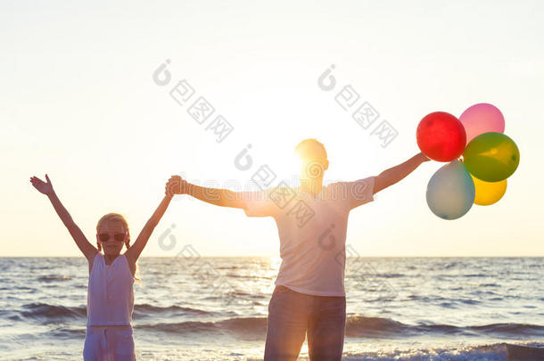 父亲和女儿在日落时在海滩上玩气球。