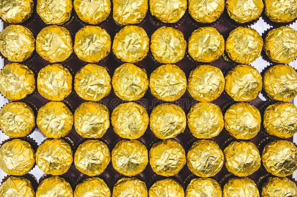 很多闪亮的金色巧克力包装纸在白色背景上排列。。
