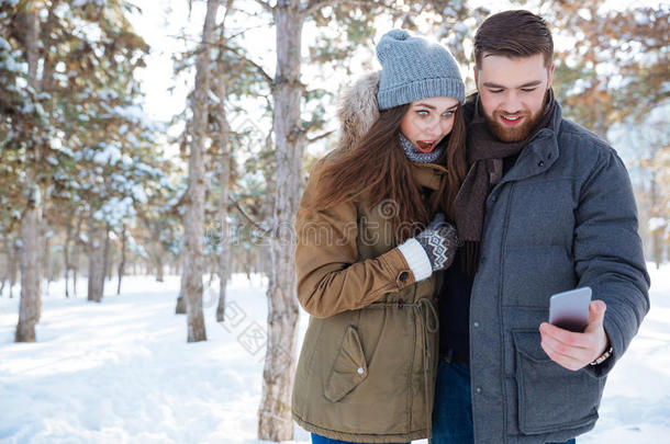 夫妇在冬<strong>季</strong>公园使用智能<strong>手机</strong>