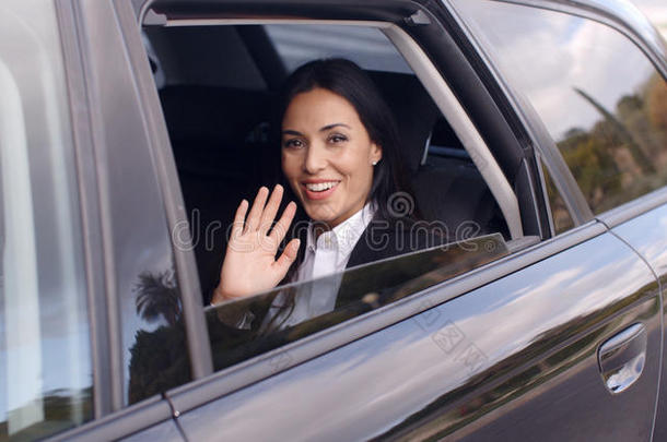 可爱的商业女人坐在车里挥舞着手