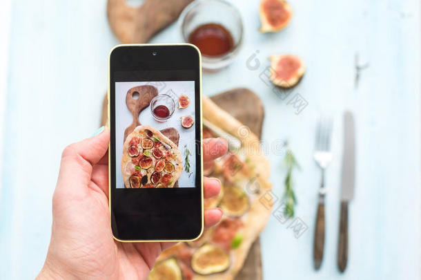 手机上的手工制作镜头：带有无花果的乡村自制披萨、烤火腿和马苏里拉奶酪、深色木制服务