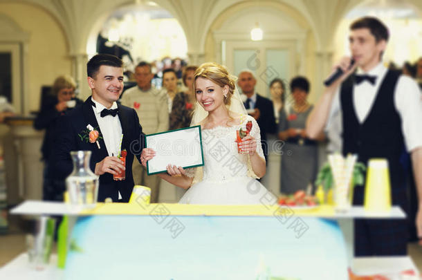 美丽的金发新娘和英俊的新郎在酒吧看台接待处持有结婚证