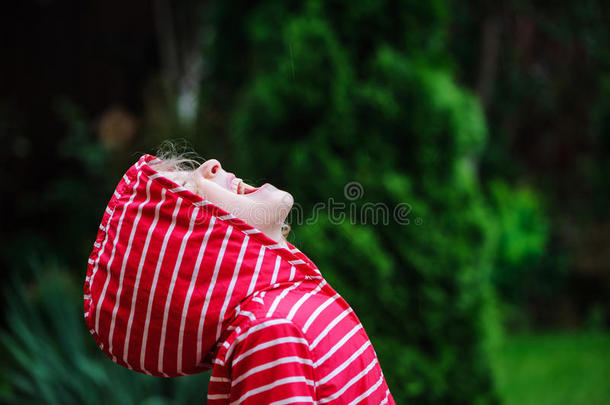 穿着红色雨衣的女孩在雨天的夏天花园里散步