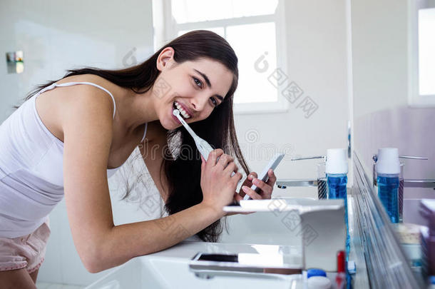 黑发女人刷牙时使用智能手机