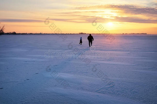 爸爸在日落时在一条冰冻的河上为她的女儿跑步。