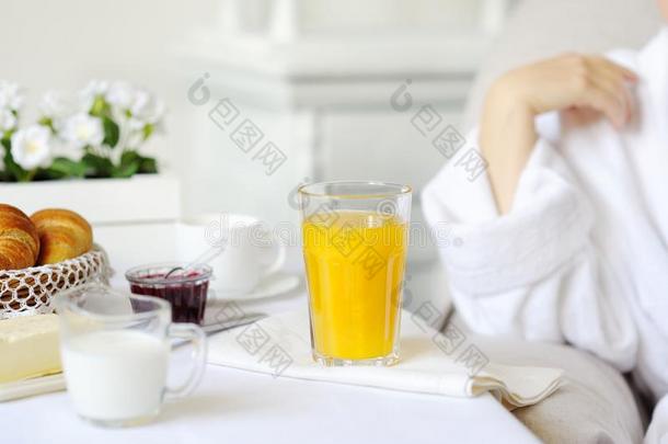 美丽的女人在一张白色的桌子后面，桌子上有新鲜的果汁牛角面包，牛奶。