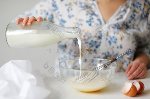 一个年轻的女人在一个打好的鸡蛋混合物倒牛奶。