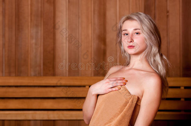 美丽的女人坐在木制桑拿棕色毛巾中放松