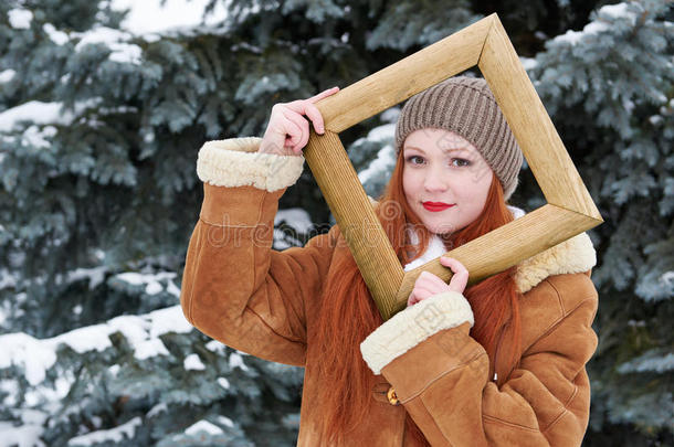 冬季木制相框中的女孩肖像。 冷杉树公园的下雪天气。