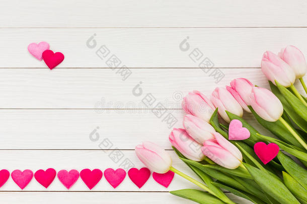 一束粉红色的郁金香在白色的木桌上装饰着心。 情人节背景