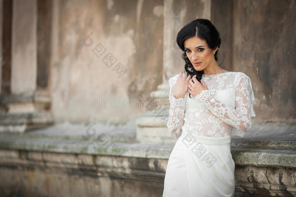 美丽的天真无邪的黑发新娘，穿着白色连衣裙，在教堂墙上摆姿势