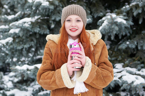女孩在冬天的公园里取暖和喝茶。 有雪的冷杉树。