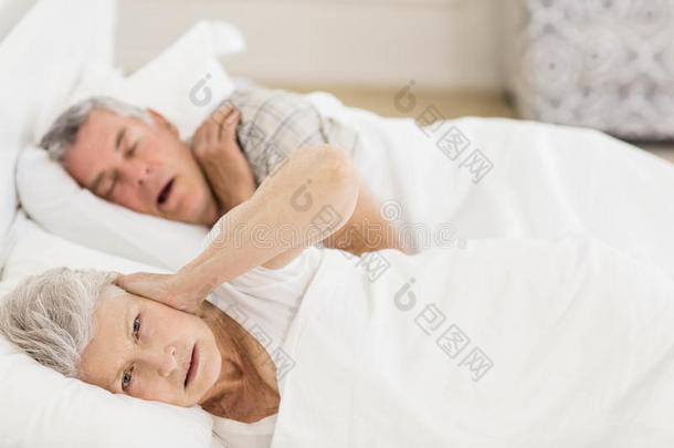 清醒的老年妇女躺在床上捂着耳朵