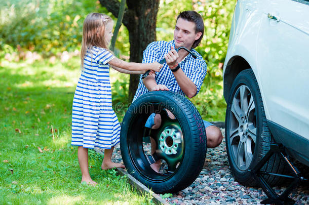 可爱的小女孩帮助父亲在美丽的夏天在户外更换汽车车轮
