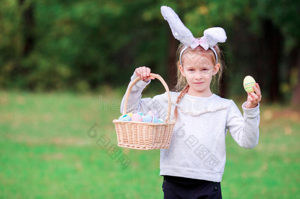 可爱的小女孩戴着兔子的耳朵，在春天拿着复活节彩蛋的篮子