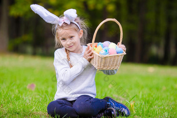 有吸引力的小女孩戴着兔子耳朵，在春天的户外，篮子里装满了复活节彩蛋