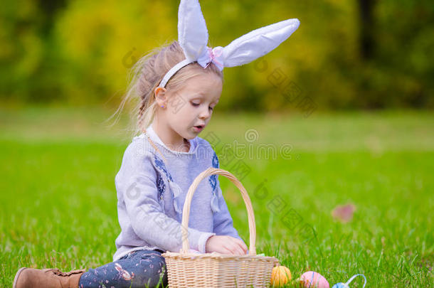 可爱的小女孩戴着兔子耳朵，在春天的户外玩复活节彩蛋