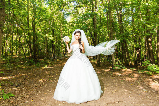 美丽的新娘穿着婚纱，带着花束和蕾丝面纱。 穿着白色婚纱的漂亮模特女孩