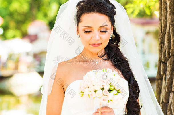 美丽的新娘穿着婚纱，带着花束和蕾丝面纱。 穿着白色婚纱的漂亮模特女孩