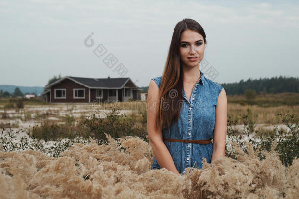 可爱的乡村女士站在高高的草地上对抗牧场的房子