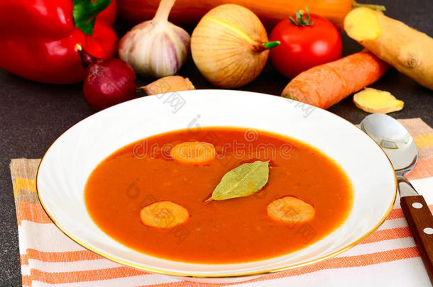 胡萝卜番茄汤在盘子里。 后面躺着汤料，蔬菜。 意大利全国美食