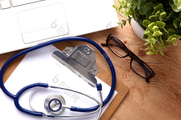 一种医疗听诊器，靠近笔记本电脑的木制桌子，白色的