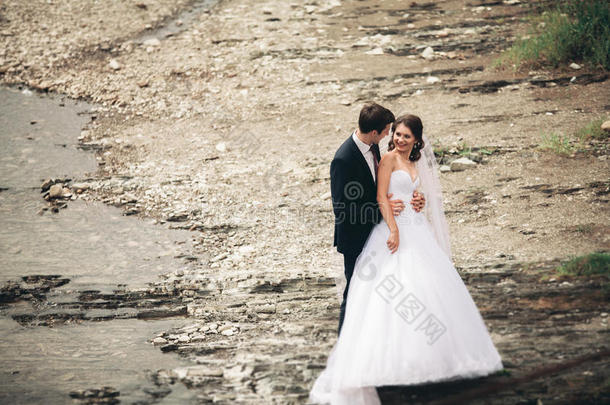 优雅，温柔，时尚，新郎和新娘靠近河边，有石头。 一对相爱的新婚夫妇