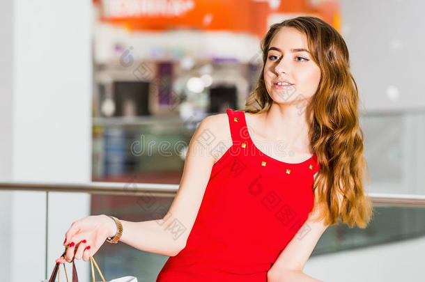 漂亮的年轻女人穿着红色连衣裙，在商场里拿着购物袋