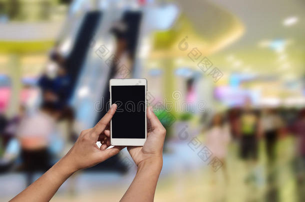 手持和触摸屏智能手机，在模糊的照片上的百货商场中心和人的背景。