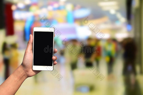 手持和触摸屏智能手机，在模糊的照片上的百货商场中心和人的背景。