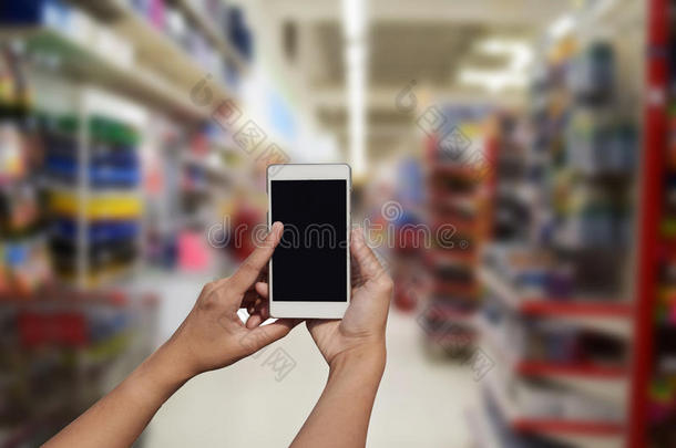 手持和触摸屏智能手机，在模糊的照片上的超市商店的背景与Bokeh。