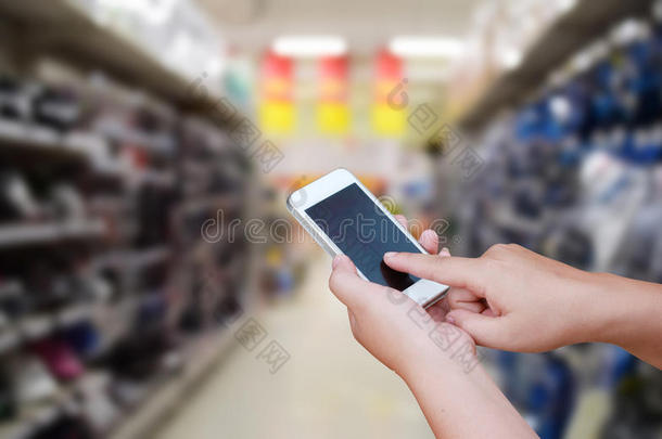 手持和触摸屏智能手机，在模糊的照片上的超市商店的背景与Bokeh。
