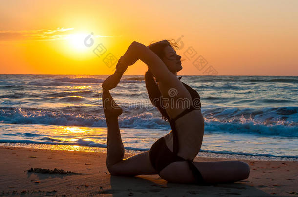 女孩正在做瑜伽，坐在一条腿的国王鸽子姿势，EkaPadaRajakapotasana在海滩上第一缕阳光