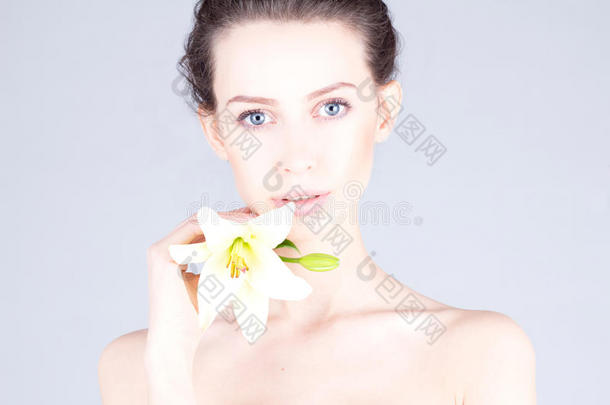 美丽的年轻女人，手里拿着一朵百合花，有着一双<strong>蓝色</strong>的<strong>大眼睛</strong>。 水疗和美容。