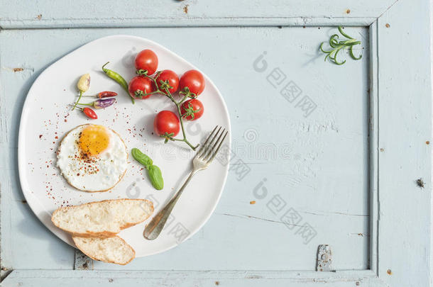 早餐套餐。 煎鸡蛋，面包片，樱桃西红柿，辣椒和草药在白色陶瓷盘子上浅蓝色