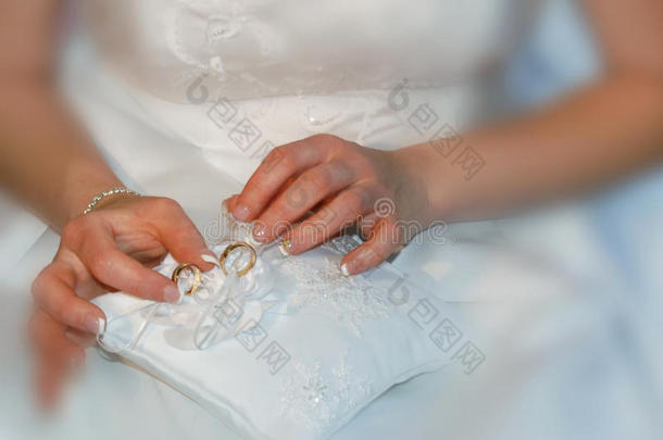 新娘拿着两个金色结婚戒指的花边垫