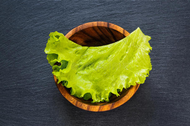 新鲜的绿色<strong>生菜叶</strong>在木碗上的黑色石板石作为模板食品背景。 顶部平面视图
