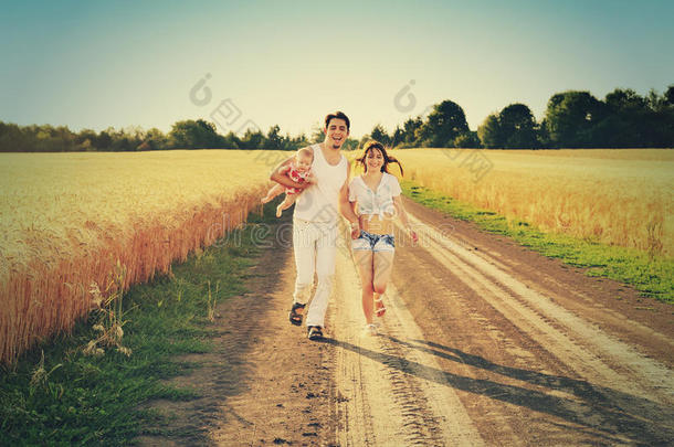一家人一起穿过夏天收获的田野。 快乐的家庭在户外一起享受和跑步。