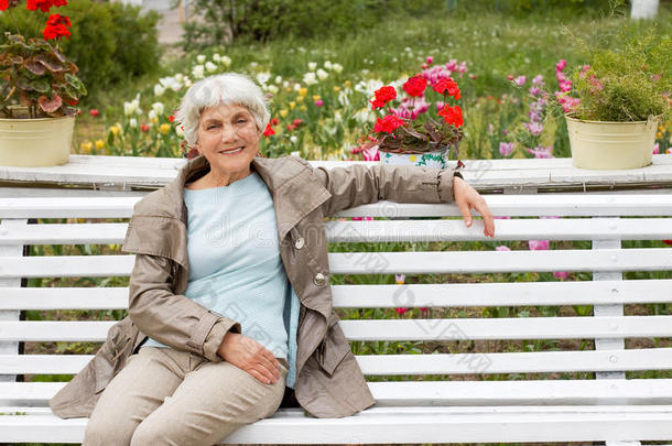 美丽可爱的老妇人坐在公园的长凳上，上面有花。