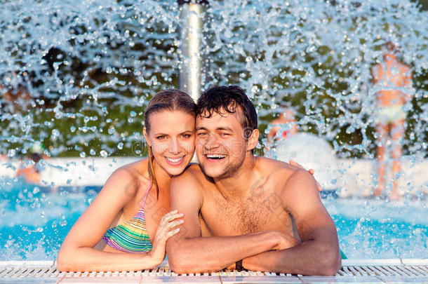 一对夫妇在飞溅喷泉下的游泳池里。 夏季炎热。
