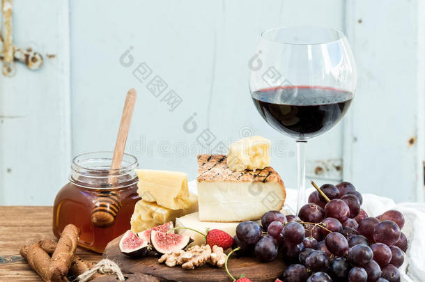 <strong>一杯红酒</strong>，奶酪板，葡萄，无花果，草莓，蜂蜜和面包棒在乡村木桌上，蓝色