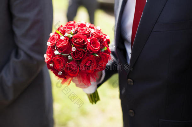 优雅时尚的新郎，红色领带，捧着华丽的红色花束