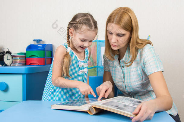 五岁的女孩和母亲在家里的桌子上看着相册里的照片