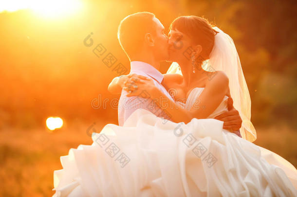 新郎在日落的背景下拥抱和亲吻他的新娘