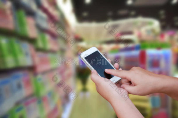 手持触摸屏智能手机，在抽象模糊图像百货商场购物中心和人群背景上。