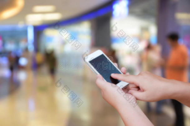 手持触摸屏智能手机，在抽象模糊图像百货商场购物中心和人群背景上。