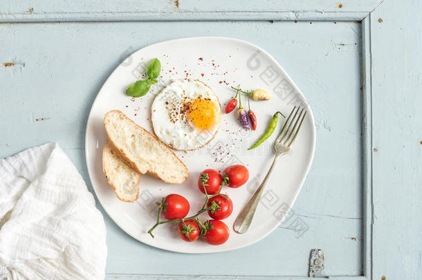 <strong>早餐</strong>套餐。 <strong>煎鸡蛋</strong>，面包片，樱桃西红柿，辣椒和草药在白色陶瓷盘子上浅蓝色