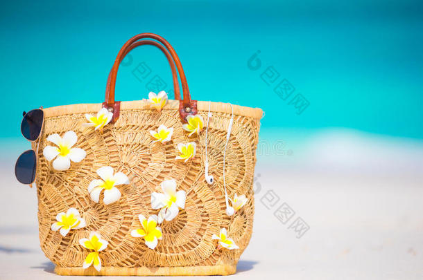 特写美丽的袋子与弗兰吉帕尼花和太阳镜在白色海滩