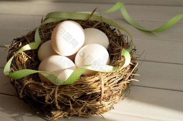 带绿色丝带的农村篮子里的复活节彩蛋。 鸡蛋在鸟巢特写。