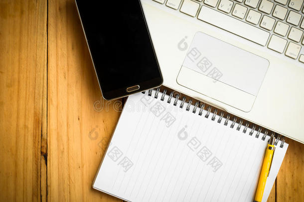 空白笔记本和一支黄色钢笔，上面有手机和笔记本电脑